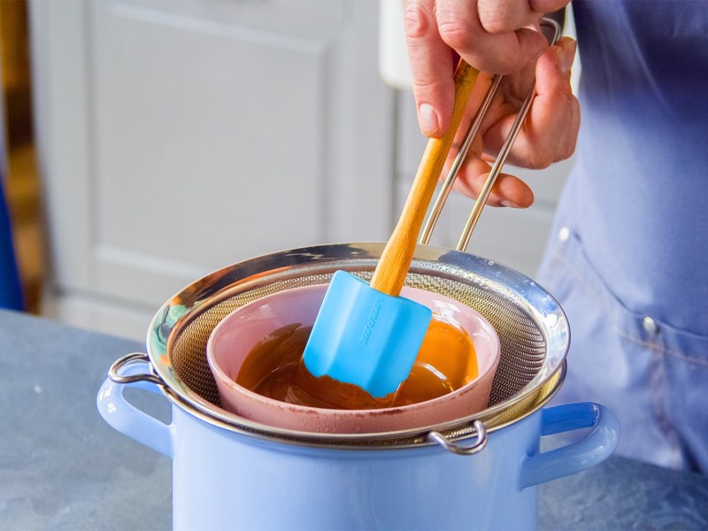 Ein Koch schmilzt Schokolade im Wasserbad mit Hilfe eines Siebs.