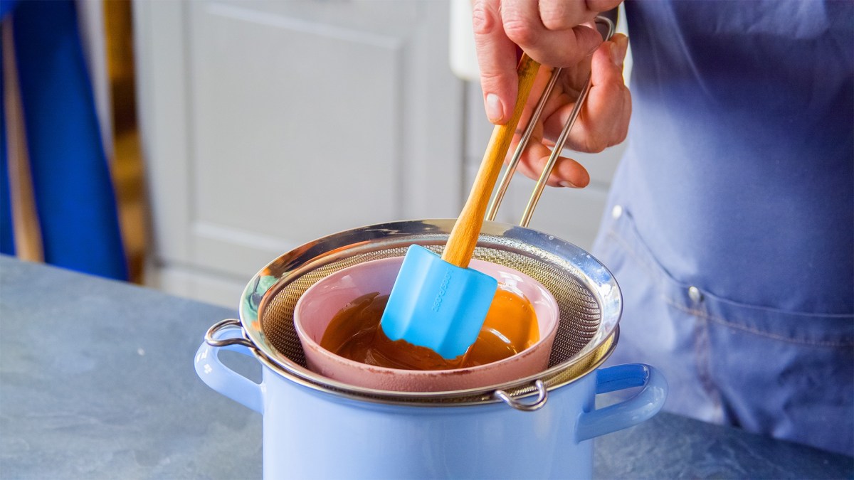 Ein Koch schmilzt Schokolade im Wasserbad mit Hilfe eines Siebs.