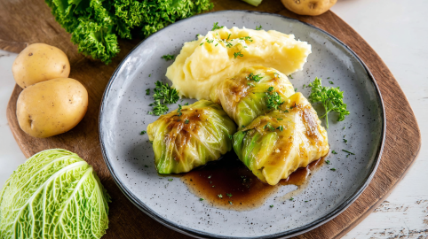 Einige Spitzkohlrouladen mit Hackfleisch auf einem Teller mit Kartoffelpüree und Bratensoße.