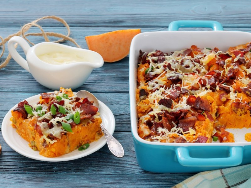 Süßkartoffelauflauf mit Pilzen, von dem bereits eine Portion entnommen wurde. Diese liegt auf einem Teller daneben.