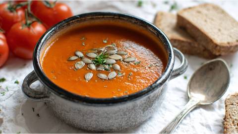 Schale mit Tomaten-Kürbissuppe, Tomaten und Scheiben Brot daneben