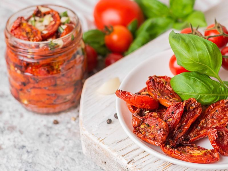 Tomaten selbst trocknen: ein Teller getrocknete Tomaten, ein Glas Tomaten mit Öl im Hintergrund.