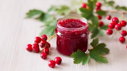 Ein Glas mit Weißdorn-Marmelade. Ringsum liegen ein paar Weißdornbeeren verteilt.