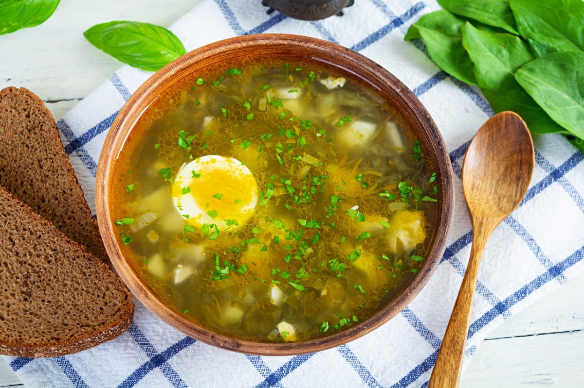 Eine Schale andalusische Hühnersuppe mit Fleisch, Eiern und Nudeln. Daneben liegt ein Löffel und zwei Scheiben Brot.