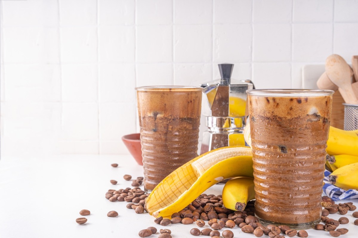 Zwei Gläser mit Bananen-Kaffee-Smoothie. Eine Banane und Kaffeebohnen liegen als Dekoration außen herum.