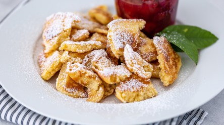 Bananen-Schmarrn mit Puderzucker und Zwetschgenkompott auf einem Teller.