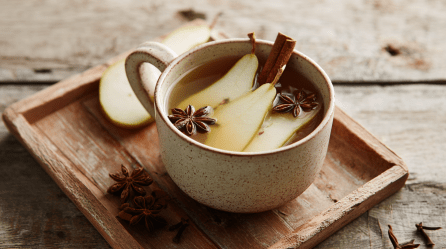 Eine Tasse Birnenpunsch auf einem kleinen Holztablett. Es liegen Birnen, Sternanis und eine Zimtstange in der Tasse.
