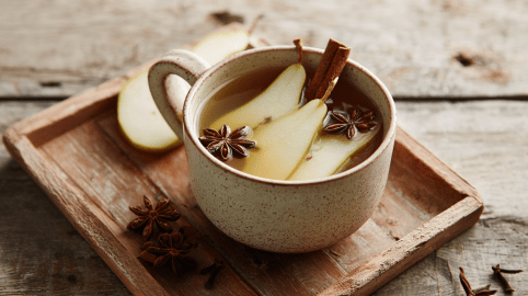 Eine Tasse Birnenpunsch auf einem kleinen Holztablett. Es liegen Birnen, Sternanis und eine Zimtstange in der Tasse.