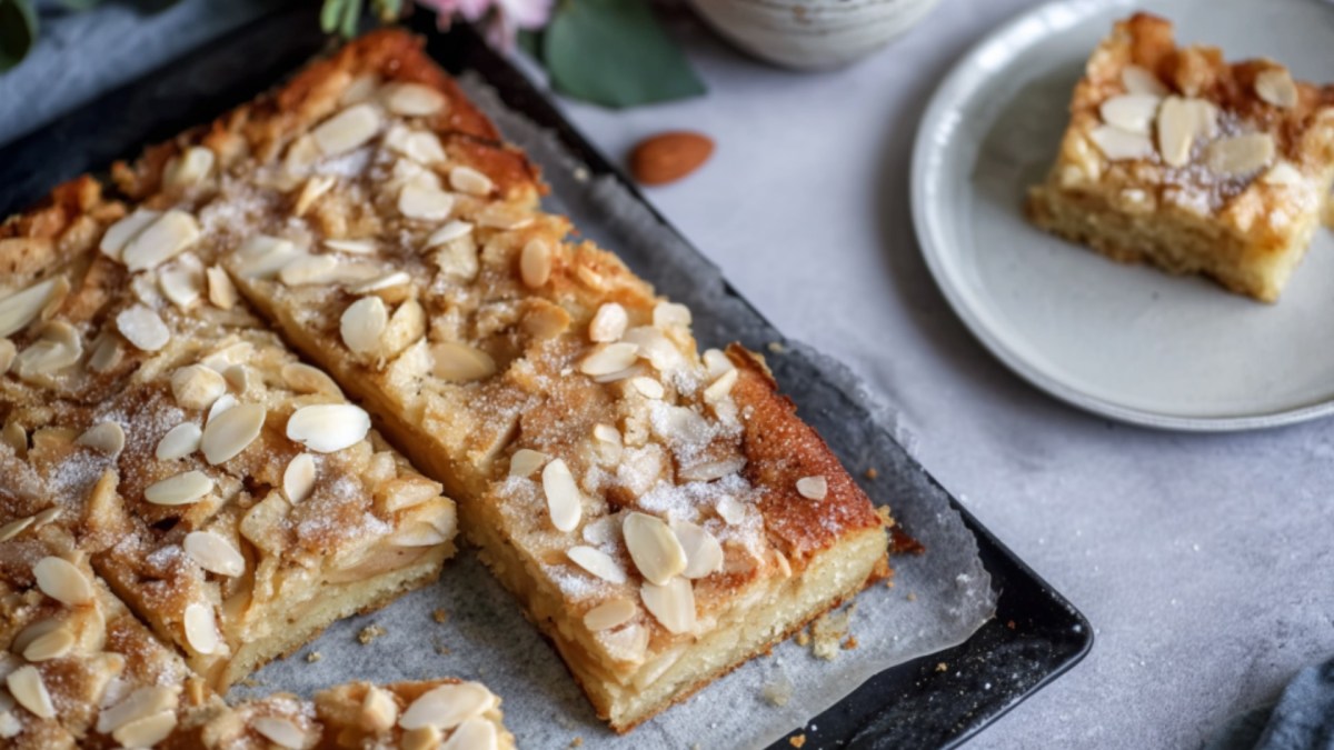Ein angeschnittener Bratapfel-Butterkuchen auf einem Blech. Ein Stück auf einem Teller daneben.
