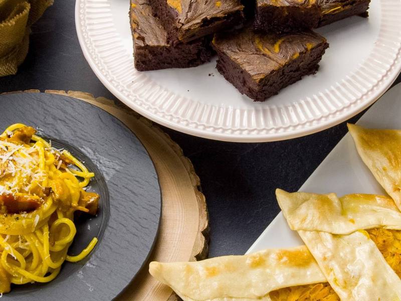 Draufsicht: ein Teller mit Kürbis-Brownies, ein Teller mit Kürbis-Carbonara, ein Teller mit Kürbis-Bolani. Eine Zutat, drei Rezepte.