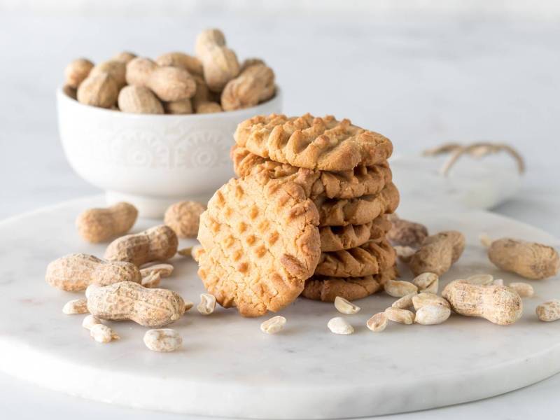 Ein Stapel mit Erdnussbutter-Miso-Cookies. Im Hintergrund steht eine Schüssel mit Erdnüssen.