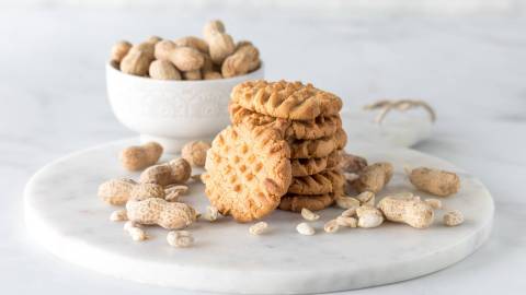 Ein Stapel mit Erdnussbutter-Miso-Cookies. Im Hintergrund steht eine Schüssel mit Erdnüssen.