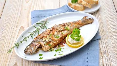 Forelle Müllerin-Art auf einem ovalen Teller, serviert mit Zitrone.