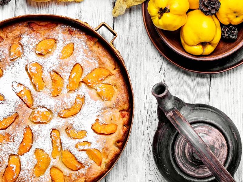 Französischer Quittenkuchen in einer Springform auf einem Tisch, Kanne und eine Schale mit Quitten daneben