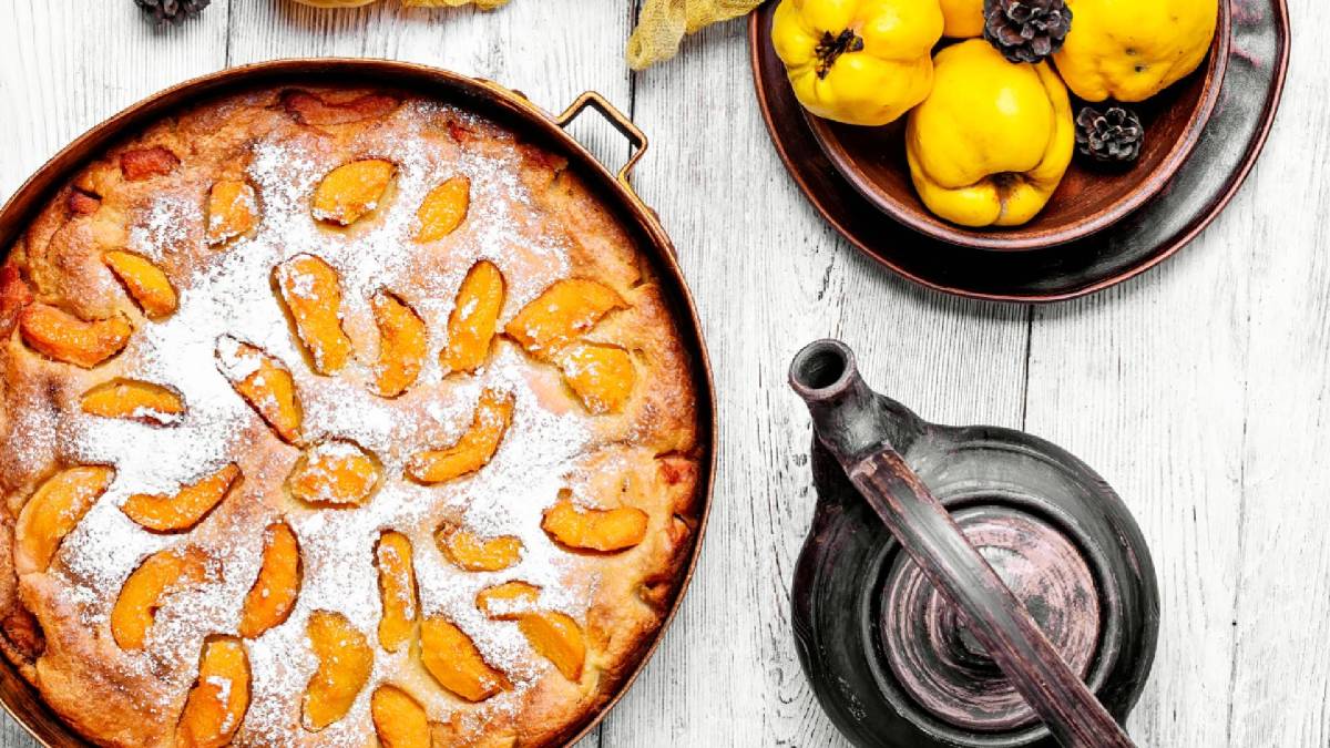 Französischer Quittenkuchen in einer Springform auf einem Tisch, Kanne und eine Schale mit Quitten daneben