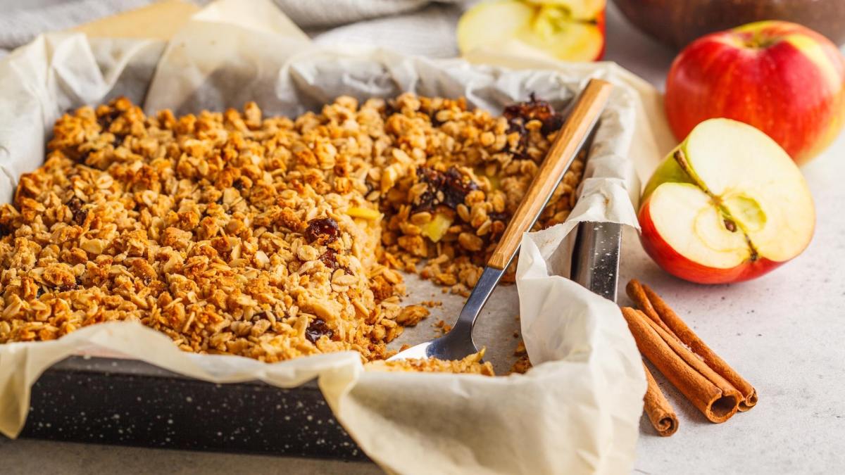 Gebackene Apfelkuchen-Haferflocken in einer Auflaufform, daneben eine Zimtstange und Äpfel.