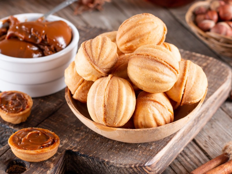 Gefüllte Nüsse, die in einer Schale übereinander liegen. Daneben steht eine Schale mit Schoko-Sahne und es liegen Zutaten.