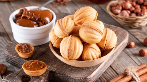 Gefüllte Nüsse, die in einer Schale übereinander liegen. Daneben steht eine Schale mit Schoko-Sahne und es liegen Zutaten.