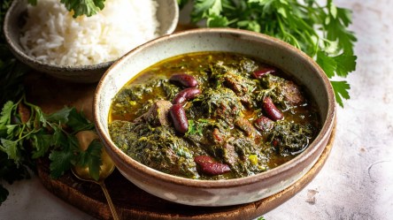 Eine Schüssel mit Ghormeh Sabzi. Dahinter eine Schüssel mit Reis. Auch frischer Koriander ist zu sehen.
