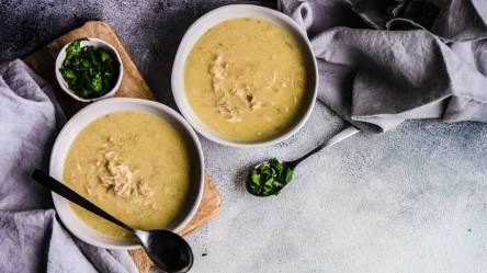 Zwei Schalen mit Chikhirtma, der georgischen Hühnersuppe auf einem Tisch, gehackter Koriander daneben