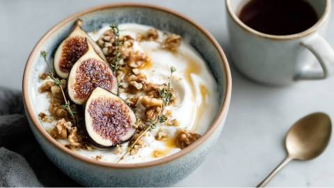 Joghurt-Bowl mit Feigen und Walnüssen, Tasse Kaffee und Löffel daneben