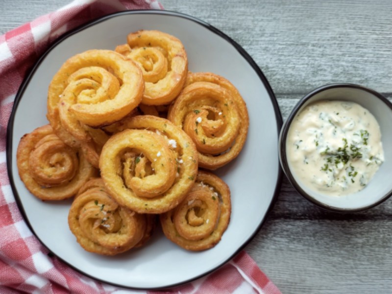 Mehrere Kartoffelwirbel auf einem Teller. Daneben steht ein Schälchen mit Dip.
