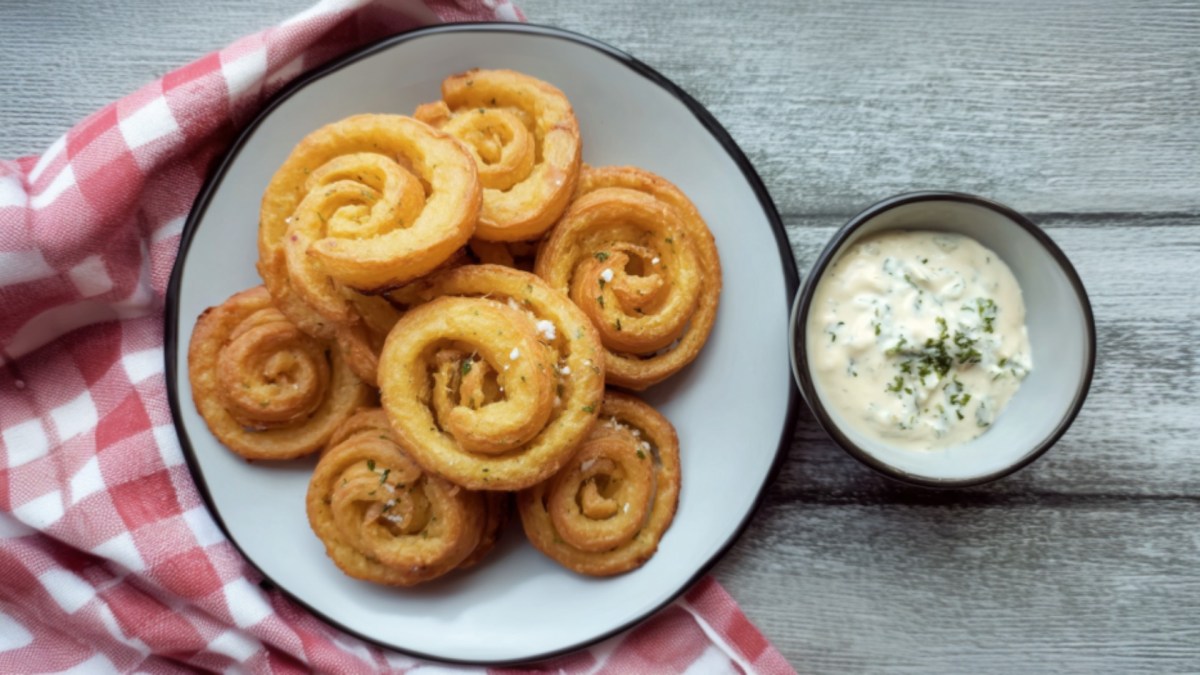 Mehrere Kartoffelwirbel auf einem Teller. Daneben steht ein Schälchen mit Dip.