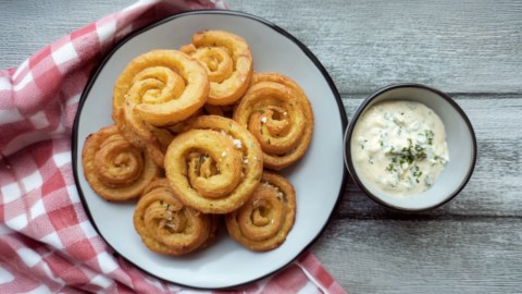 Mehrere Kartoffelwirbel auf einem Teller. Daneben steht ein Schälchen mit Dip.
