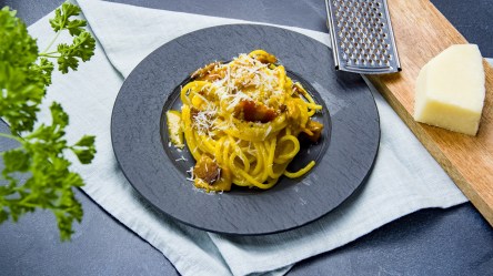 Ein Teller mit Kürbis-Carbonara. Daneben liegt ein Stück Hartkäse und eine Käsereibe.