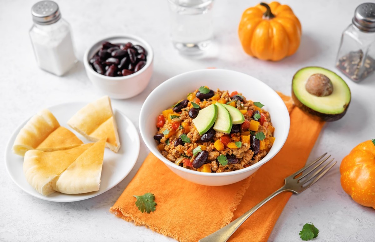 Ein Teller mit Kürbis Hähnchen Chili, garniert mit Avocadospalten. Bunte Deko außen herum.