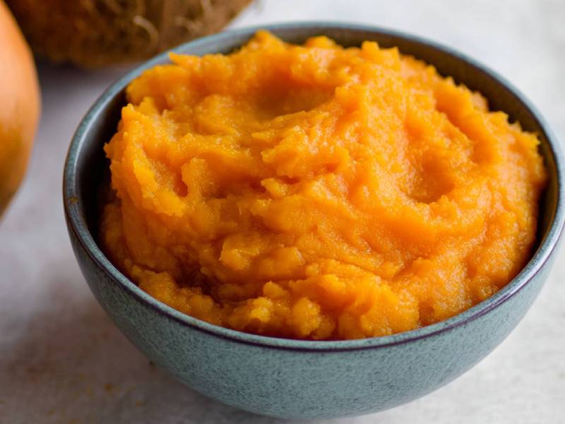 Schale mit Kürbis-Kokos-Püree, Kürbis und Kokosnuss im Hintergrund