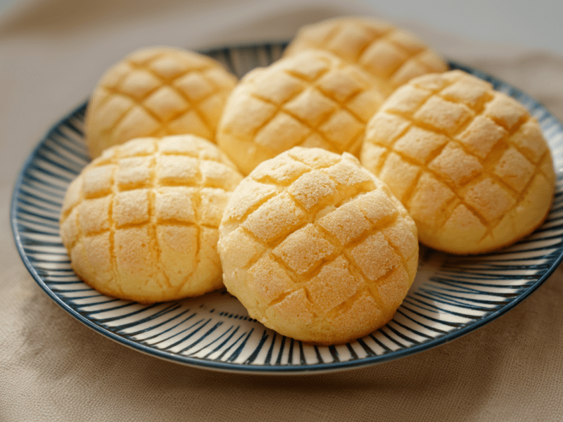 Sechs Melonpan liegen auf einem blau-weiß-gestreifen Keramikteller.