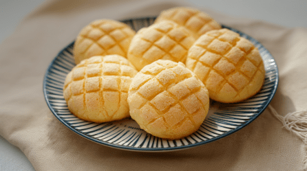 Sechs Melonpan liegen auf einem blau-weiß-gestreifen Keramikteller.