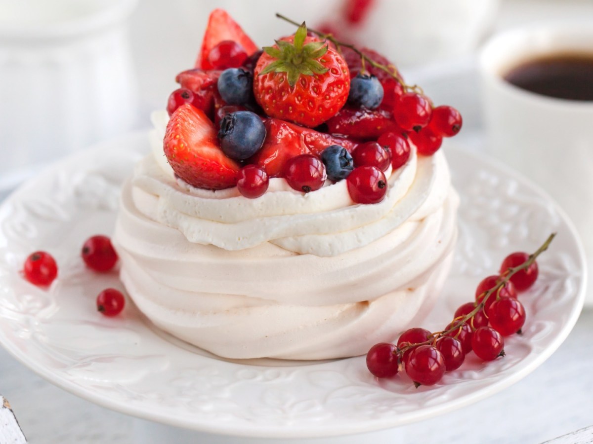 Eine Mini-Pavlova mit Beeren. Daneben steht eine Tasse Kaffee.