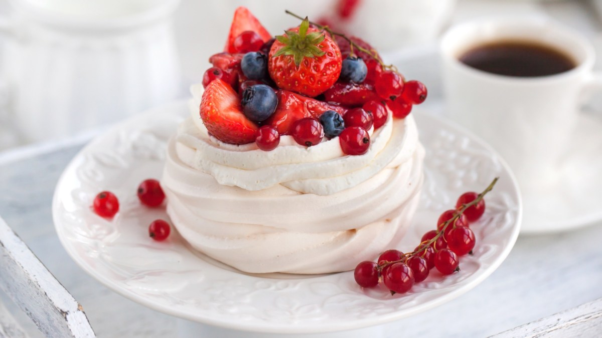 Eine Mini-Pavlova mit Beeren. Daneben steht eine Tasse Kaffee.