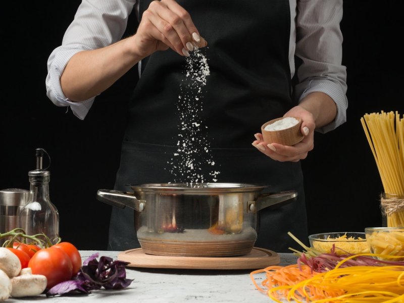 Nudeln richtig salzen: eine kochende Person salzt Nudelwasser.