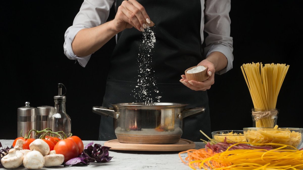 Nudeln richtig salzen: eine kochende Person salzt Nudelwasser.
