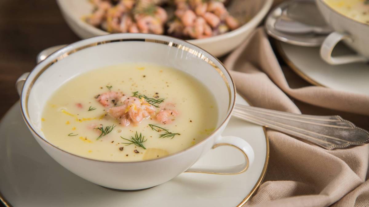 Eine Suppenschale mit ostfriesischer Krabbensuppe, die auf einem Unterteller steht, auf dem auch ein Löffel liegt. Im Hintergrund ist noch eine Schüssel mit Krabben zu sehen.