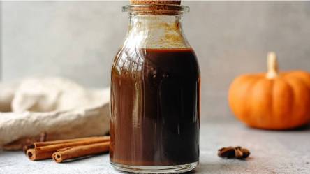 Pumpkin Spice Sirup auf einem Tisch, Kürbis und Zimtstangen daneben