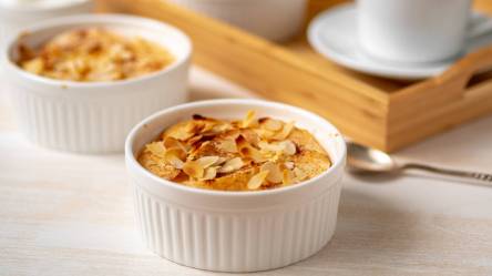 Eine kleine runde Form mit Quark-Grießauflauf mit Äpfeln. Im Hintergrund steht nochmal eine kleine Form sowie ein Tablett mit einer Kaffeetasse.