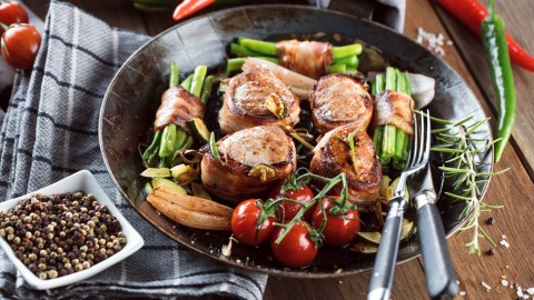 Schweinefilet im Speckmantel mit Ofengemüse und Bohnen im Speckmantel auf einem Teller.