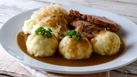 Mehrere Thüringer Klöße mit Sauerkraut, Soße und Fleisch auf einem Teller.