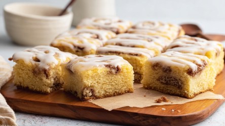 Mehrere Stücke Zimtschneckenkuchen vom Blech auf einem Holzbrett.