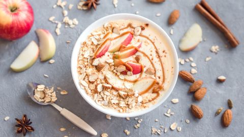Eine Schale Apple-Crumble-Grießbrei, daneben Gewürze und Äpfel.