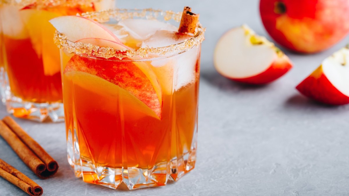 Mehrere Gläser mit Autumn Glow Cocktail, garniert mit Zimtstangen und Apfelspalten.