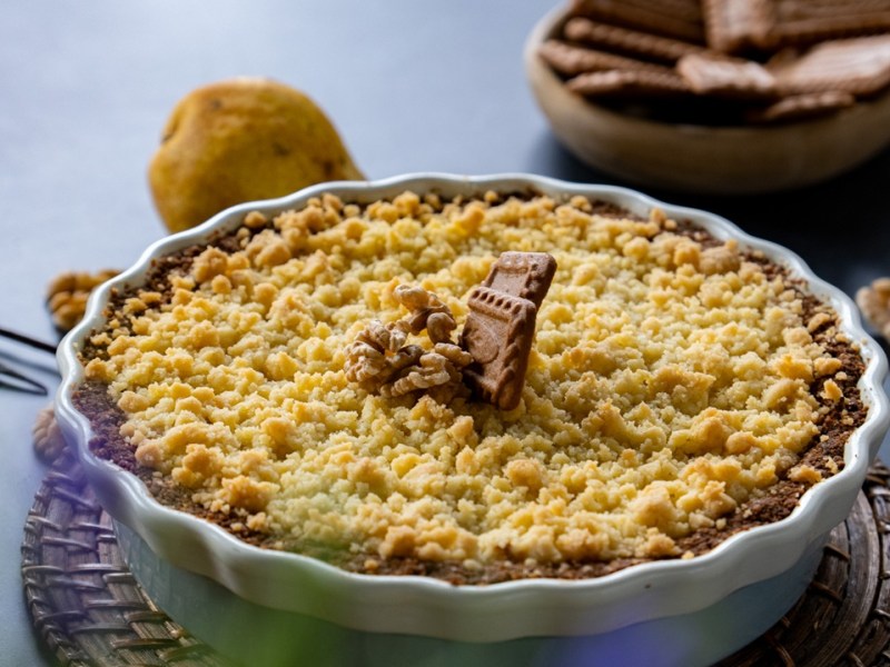 Eine Tarteform mit Birnen-Crumble mit Ziegenkäse garniert mit Walnüssen und Karamell-Keksen.