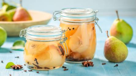 Zwei Gläser mit eingekochten Birnen und frischen Birnen daneben