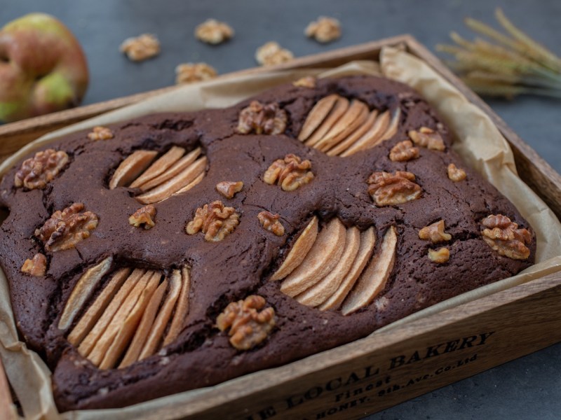 Ein Blech mit Birnen-Walnuss-Brownies. Eine Birne liegt im Hintergrund.