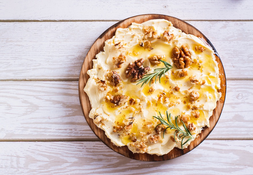 Ein Holzbrett mit Butter mit karamellisierten Walnüssen, Honig und Rosmarin.