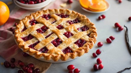 Ein Cranberry Pie, der auf einer Arbeitsfläche umgeben von frischen Cranberrys Orangen(-scheiben) und Vanilleschoten steht.